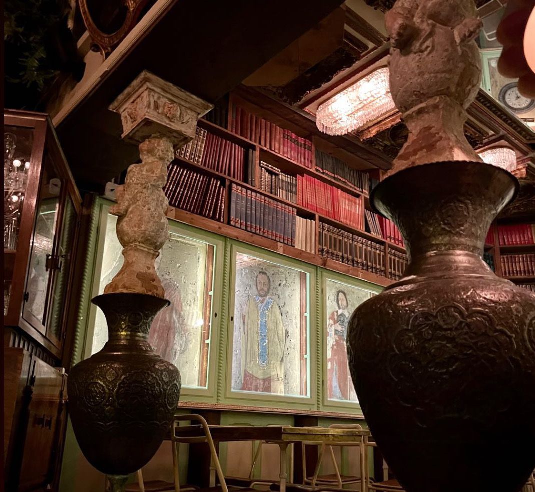 A themed room in Milan's Sacrestia Farmacia Alcolica, featuring unique ceiling pillars, a library, and fake-rusted chairs 