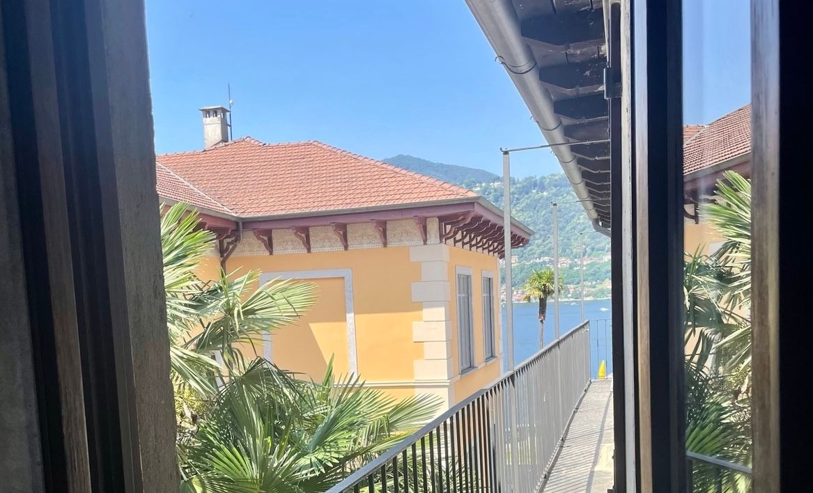 An open hotel room door leading to a balcony looking over Lake Orta. 