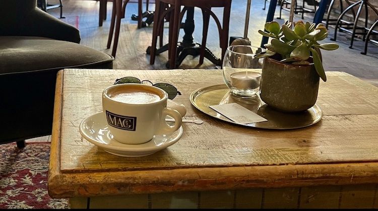 A cappuccino in a "Mag Cafe" cup sits on a wooden table inside Mag Cafe in Navigli, Milan.