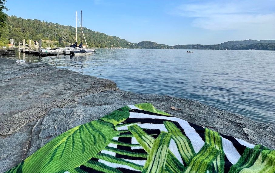A beach towel lies on a rock, looking out over the water of Lake Orta.