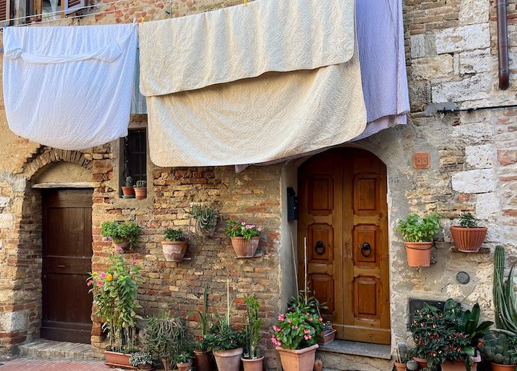 A home in Cortona, Italy. Potted flowers line the perimeter of the brick house, and sheets dry on the line above.