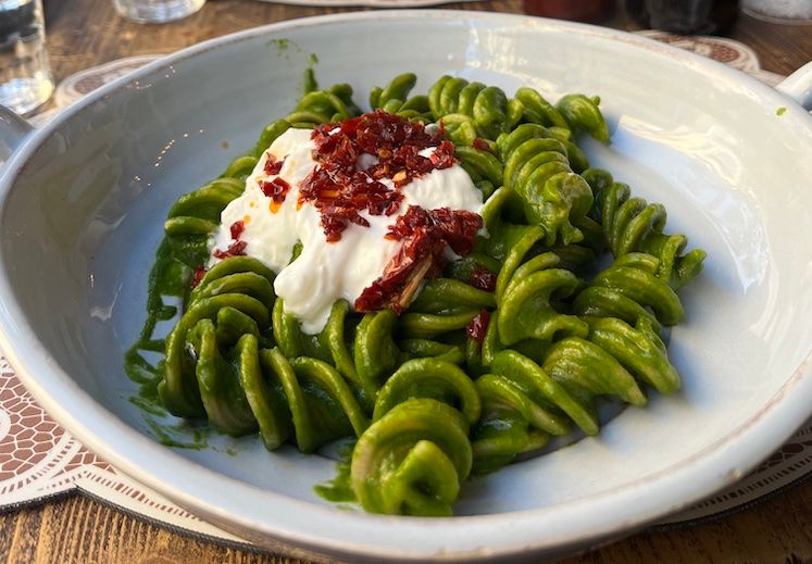 A bowl of pesto pasta with burrata cheese and sun dried tomatoes.