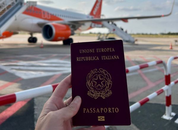 An Italian passport shown in front of a plane.