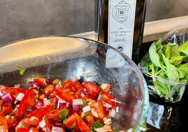 A bowl of bruschetta next to a bottle of olive oil and some basil.